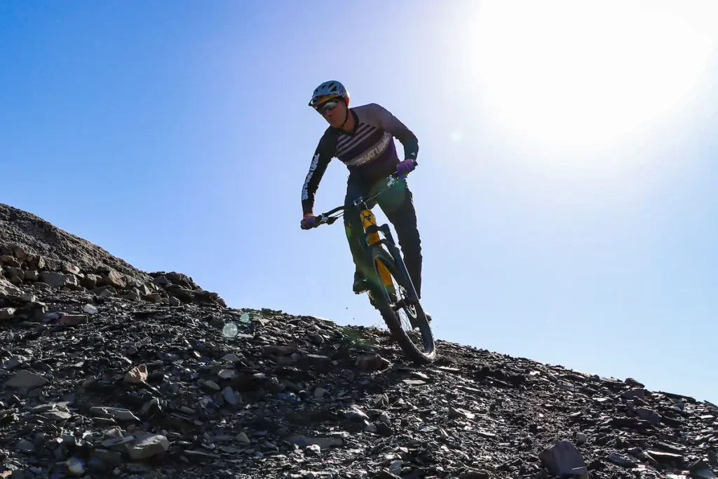 Our mtb guide Stefano mountain biker riding a yellow enduro bike down a rocky mountain ridge under a bright sun, representing Trails Unlimited MTB tours