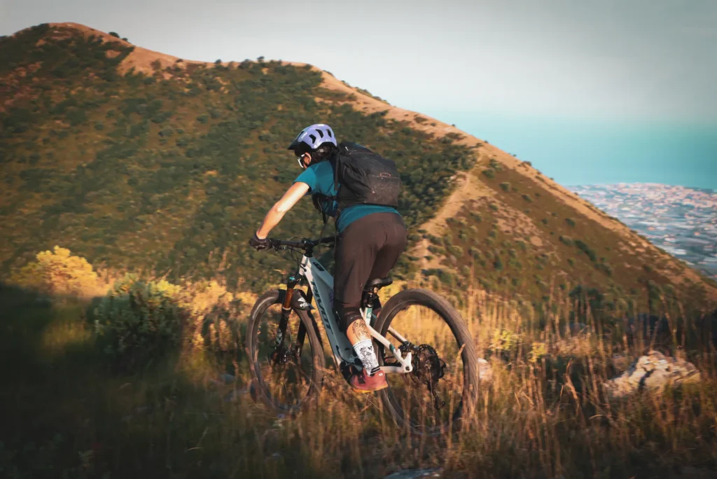 Manuela on an e-MTB climbing a scenic coastal trail during the Azur Tour by Trails Unlimited.