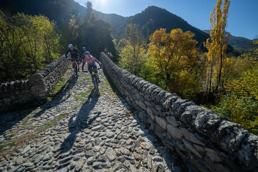 MTB riders crossing an ancient stone bridge in the Italian Alps during the Bicknell Ciclovia tour with Trails Unlimited.