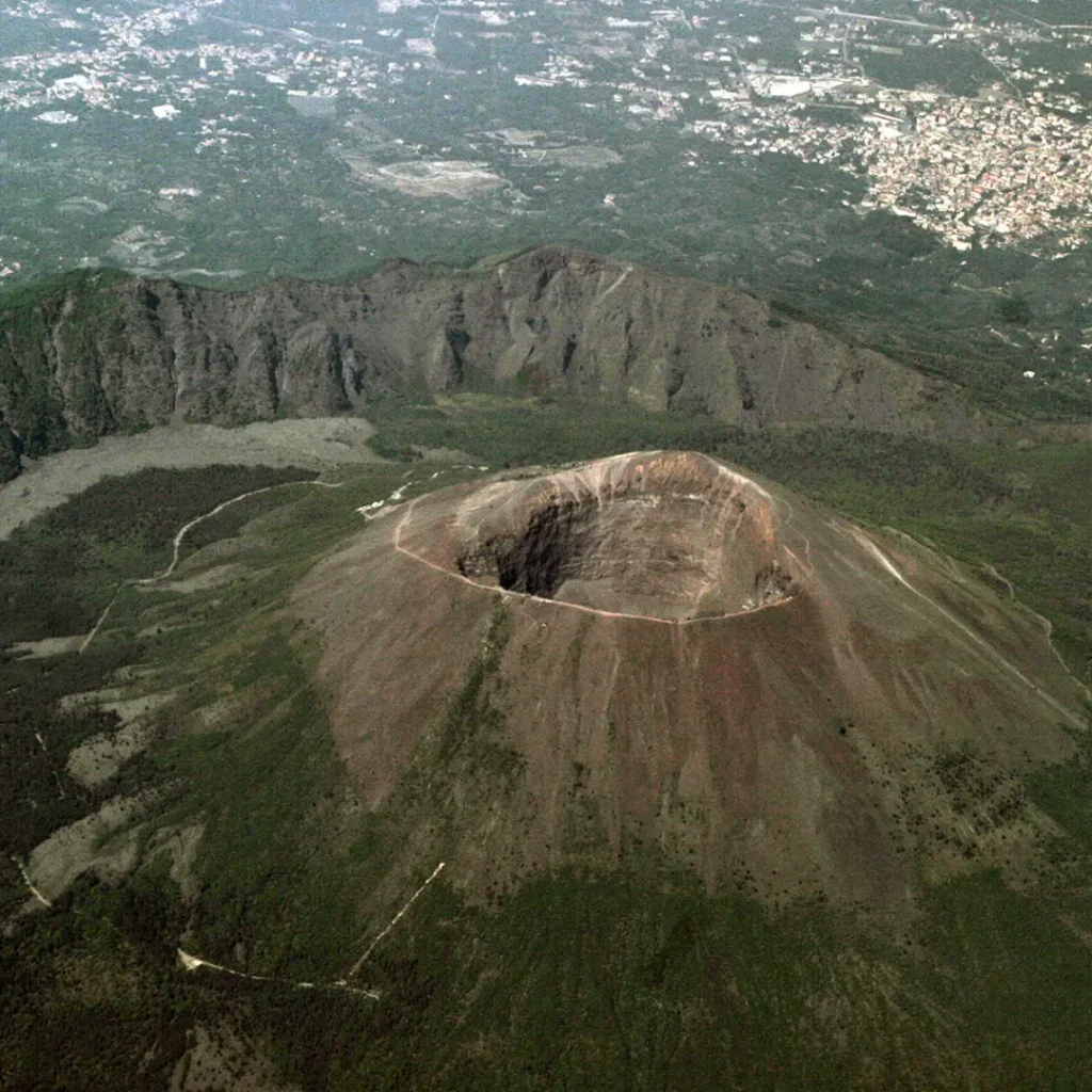 Aerial view of the Great Cone of Mount Vesuvius with its deep crater and lush green slopes, overlooking the city of Naples during the Riding into the Lava tour