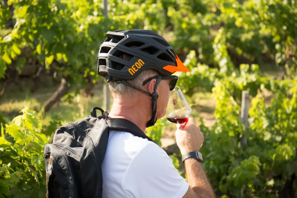 Close-up of a mountain biker tasting a glass of local red wine in a Langhe vineyard during a Trails Unlimited bike and wine tour.
