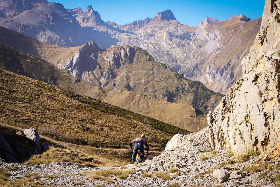 Professional MTB guide Stefano from Trails Unlimited riding through a massive rocky canyon during the Sky to Sea tour. The majestic alpine peaks in the background highlight the epic scale of this high-altitude mountain bike adventure.