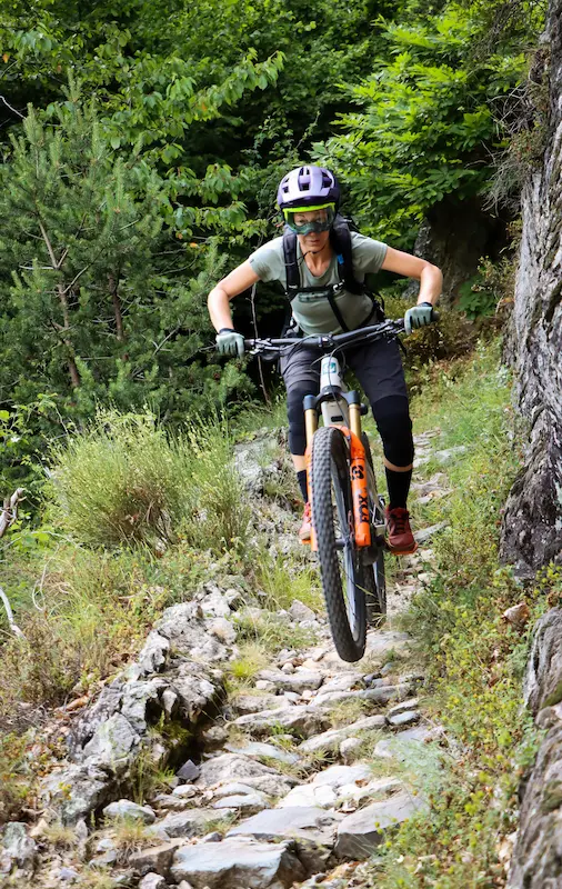 Professional female MTB guide maneuvering a technical rocky descent during the Sky to Sea tour in the Ligurian mountains