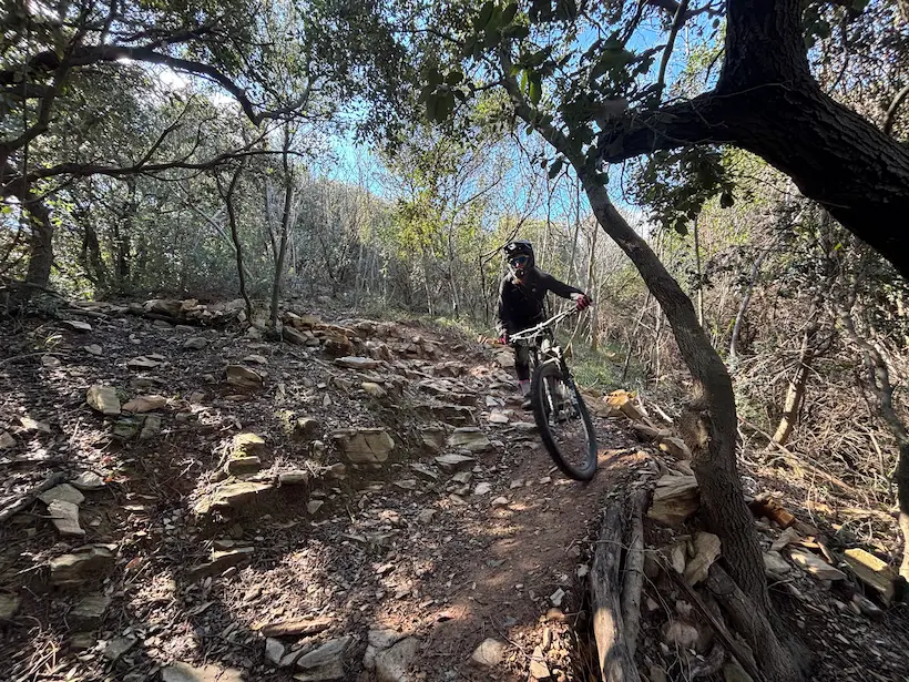 Action shot of a rider tackling a steep, challenging rock section on a classic MTB trail in the hills above Finale Ligure, Italy.
