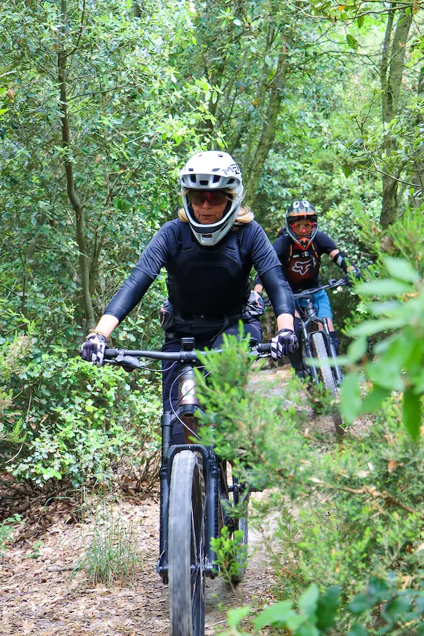 Two riders on the Bordighera E-MTB Tour navigating a narrow singletrack trail through a lush green forest on the Riviera Express route.