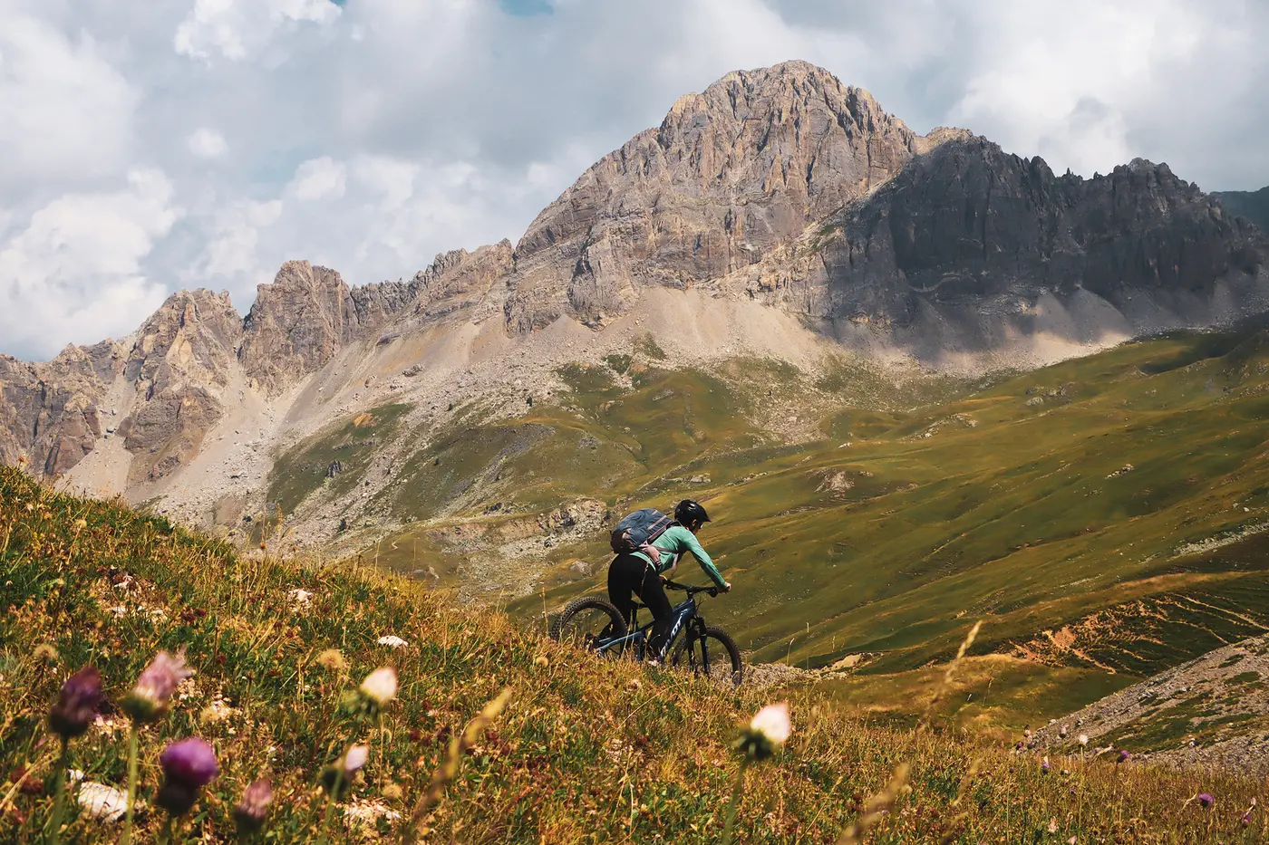 Mountain biker descending through high-altitude meadows on the Sky to Sea MTB Tour in the Italian Alps