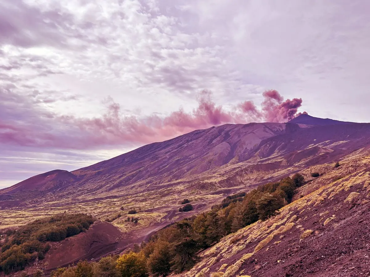 Mount Etna releasing a plume of ash above volcanic slopes and autumn woodland in Sicily.